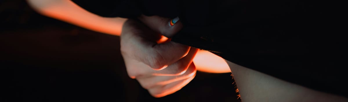 A hand, with pride nail varnish, lifts a piece of fabric on another body part